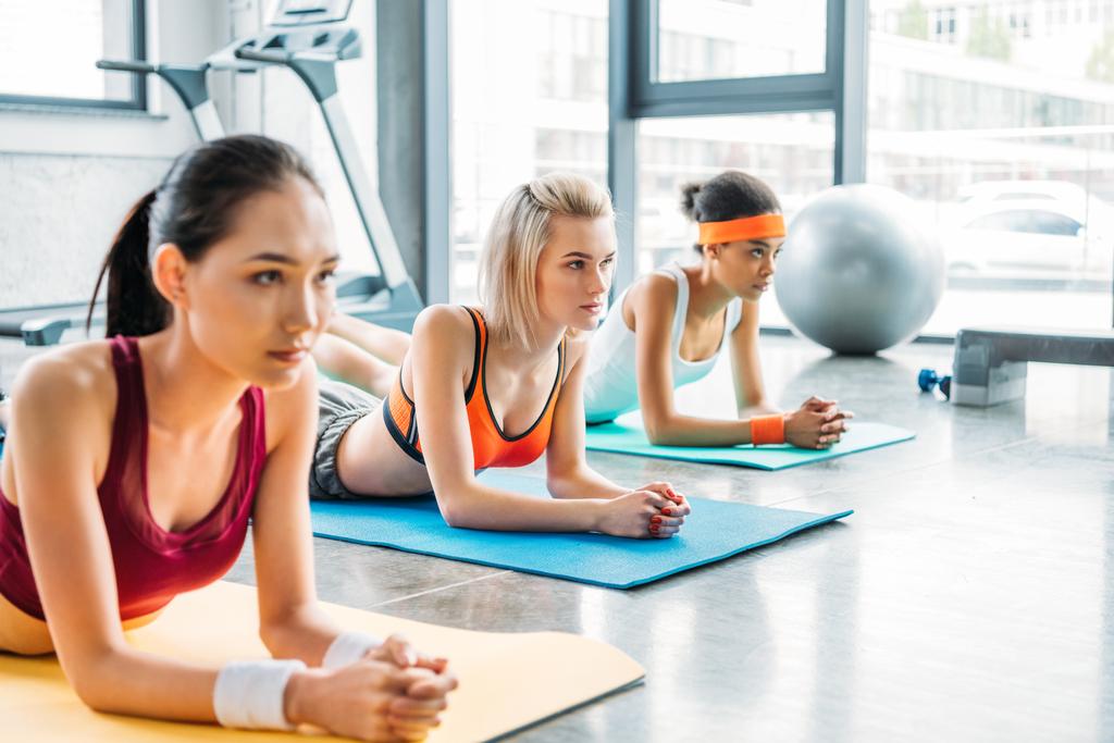 atletas multiculturais do sexo feminino se exercitando em tapetes de fitness no ginásio
 - Foto, Imagem