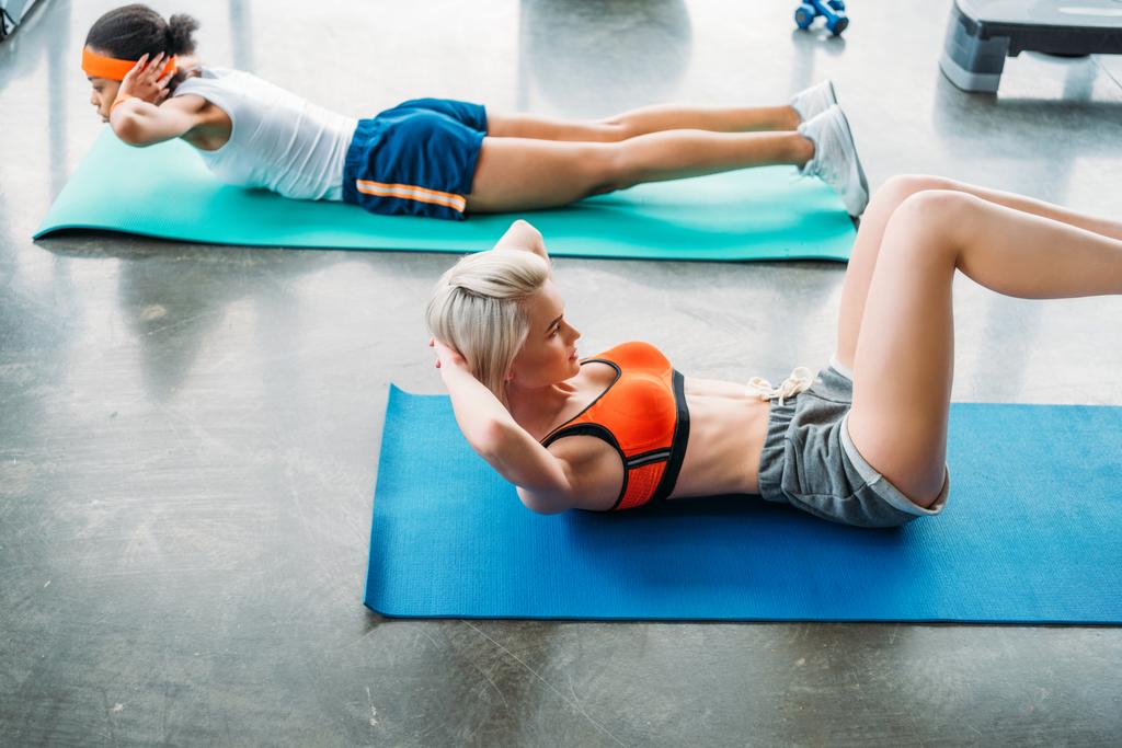 duas esportistas multiculturais atraentes que se exercitam em tapetes de fitness no ginásio
  - Foto, Imagem