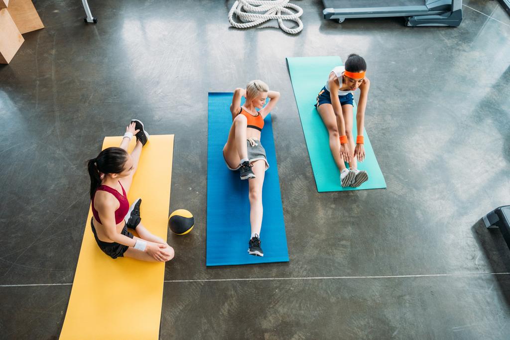 vista de alto ângulo de três esportistas multiétnicos que se exercitam em tapetes de fitness no ginásio
 - Foto, Imagem