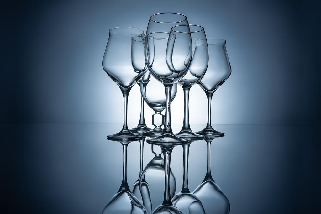 σιλουέτες των διαφορετικών άδειο ποτήρια κρασιού με αντανακλάσεις, σε γκρι - Φωτογραφία, εικόνα
