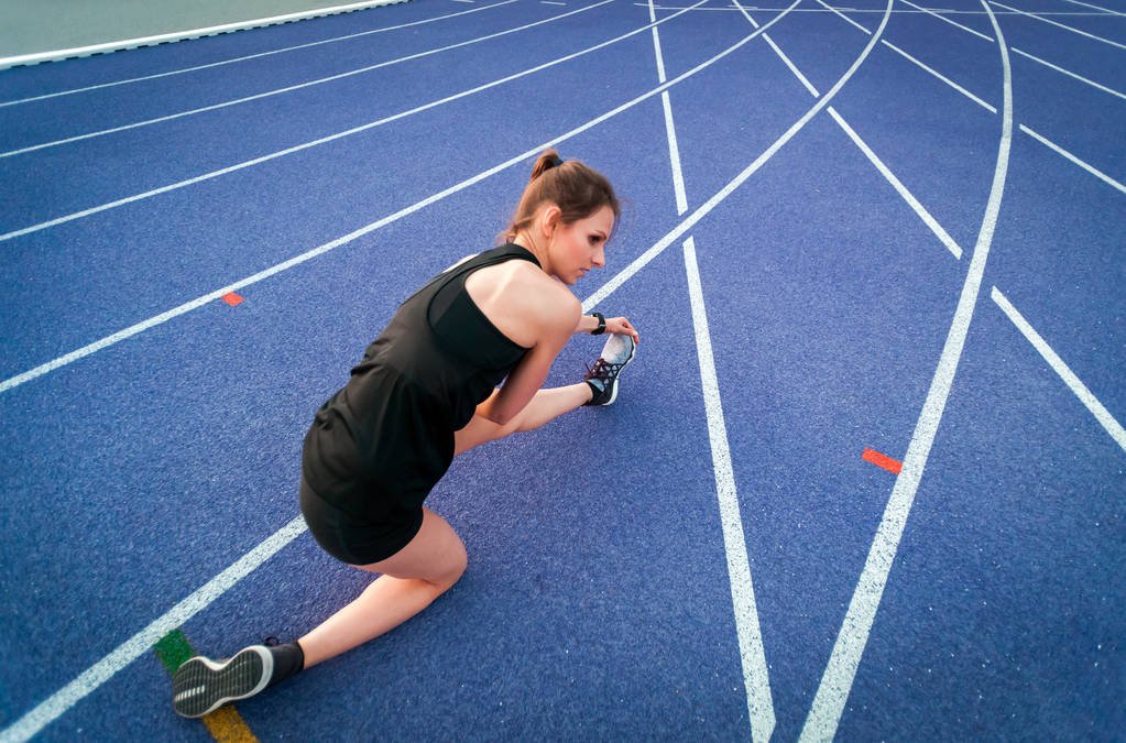 nuori urheilullinen nainen venyttely stadionilla juoksuradalla ennen lenkkeilyä
  - Valokuva, kuva