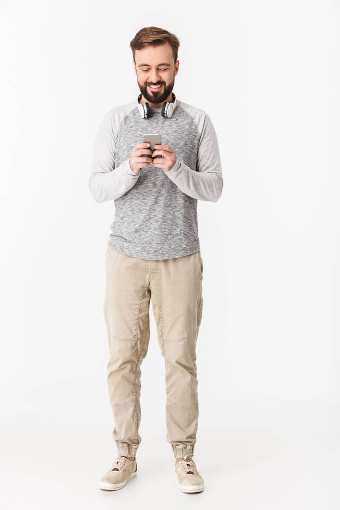 Фото усміхненого молодого чоловіка ізольовано на білому тлі стіни за допомогою мобільного телефону, який дивиться вбік
. - Фото, зображення
