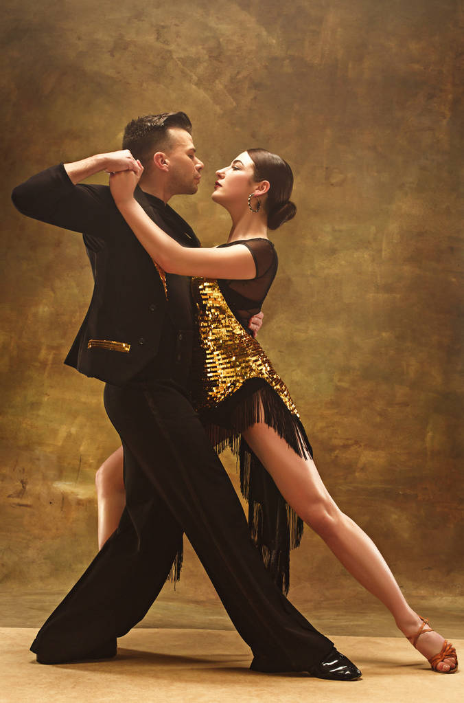 Танцевальная пара в золотом платье танцует на фоне студии
. - Фото, изображение