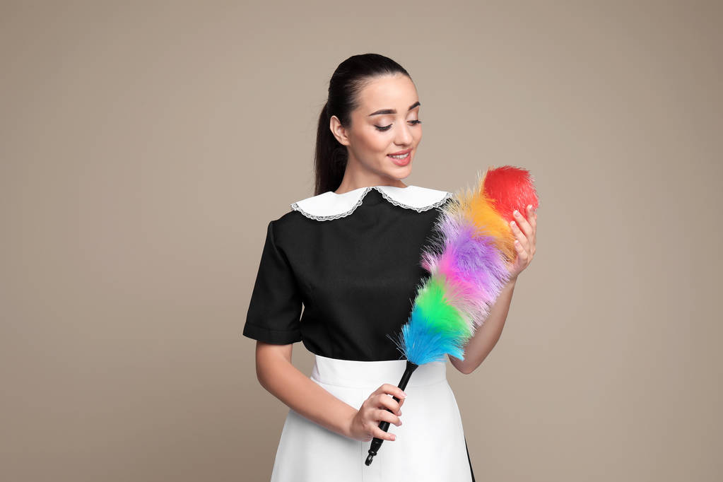 Camarera joven con cepillo de espolvoreo sobre fondo de color
 - Foto, imagen