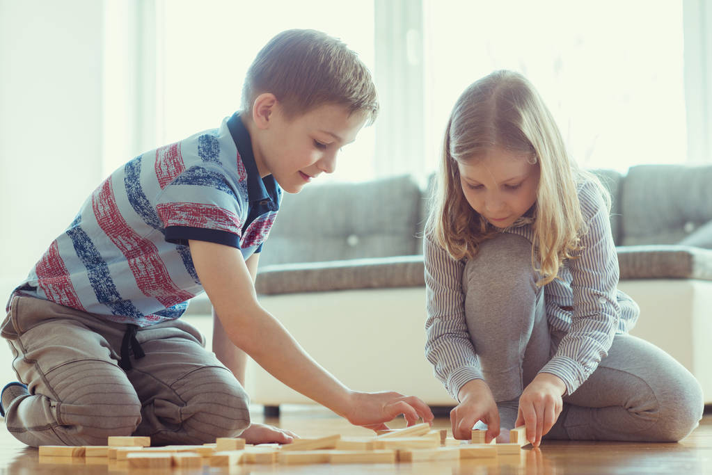 Dois irmãos felizes jogando um jogo com blocos de madeira em casa alegremente
  - Foto, Imagem