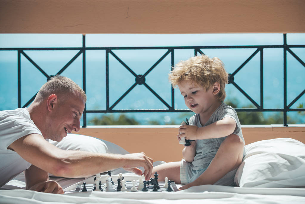 Мужчина учит мальчика правилам шахмат - играет на полу балкона
 - Фото, изображение