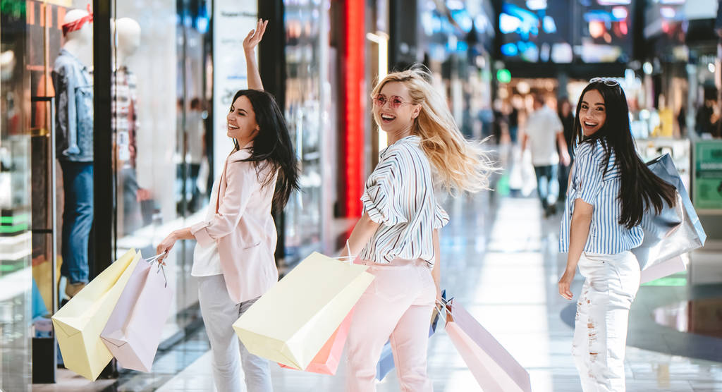 Three attractive young girls are doing shopping with shopping bags in modern mall. - Photo, Image