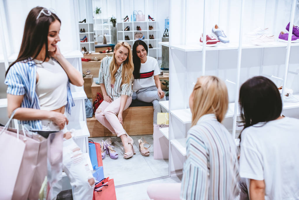 Három vonzó fiatal lányok csinálás vásárlás a cipő bolt-modern Mall bevásárló táskák. - Fotó, kép