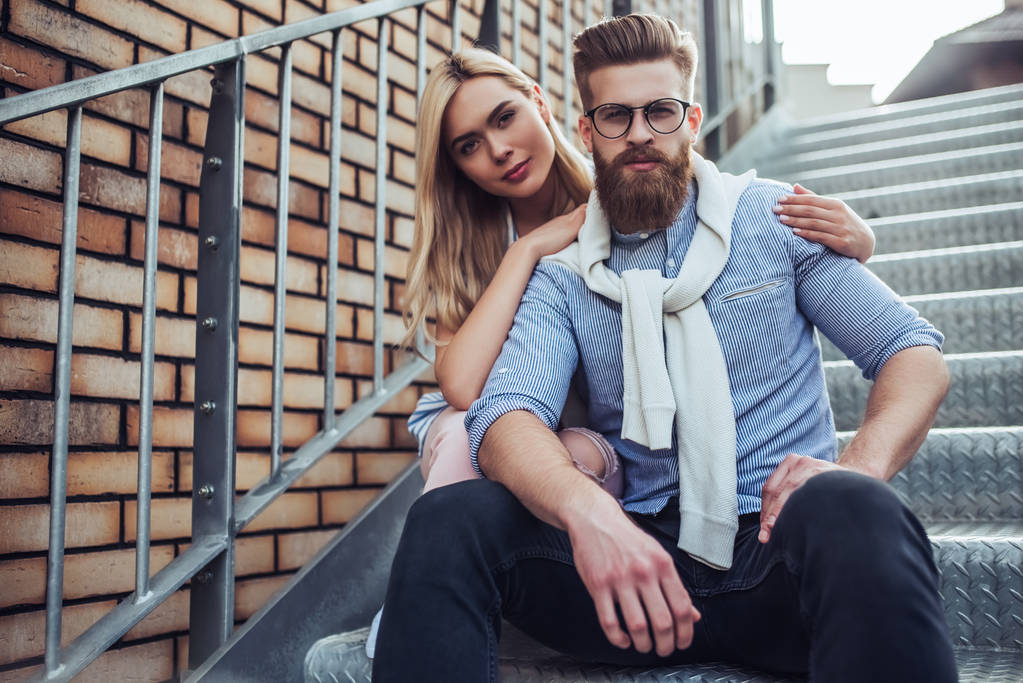 Mladé stylové šťastný pár je spolu trávili čas venku. Atraktivní žena a vousatý muž sedí na schodech ve městě. - Fotografie, Obrázek