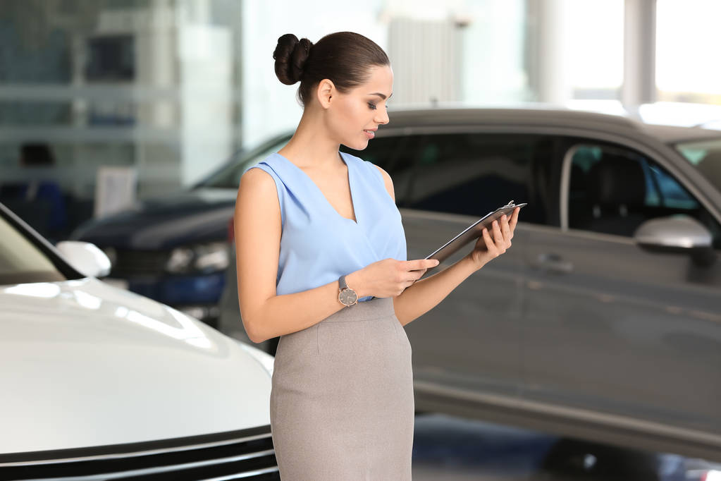 Young saleswoman with clipboard in car dealership - Photo, Image