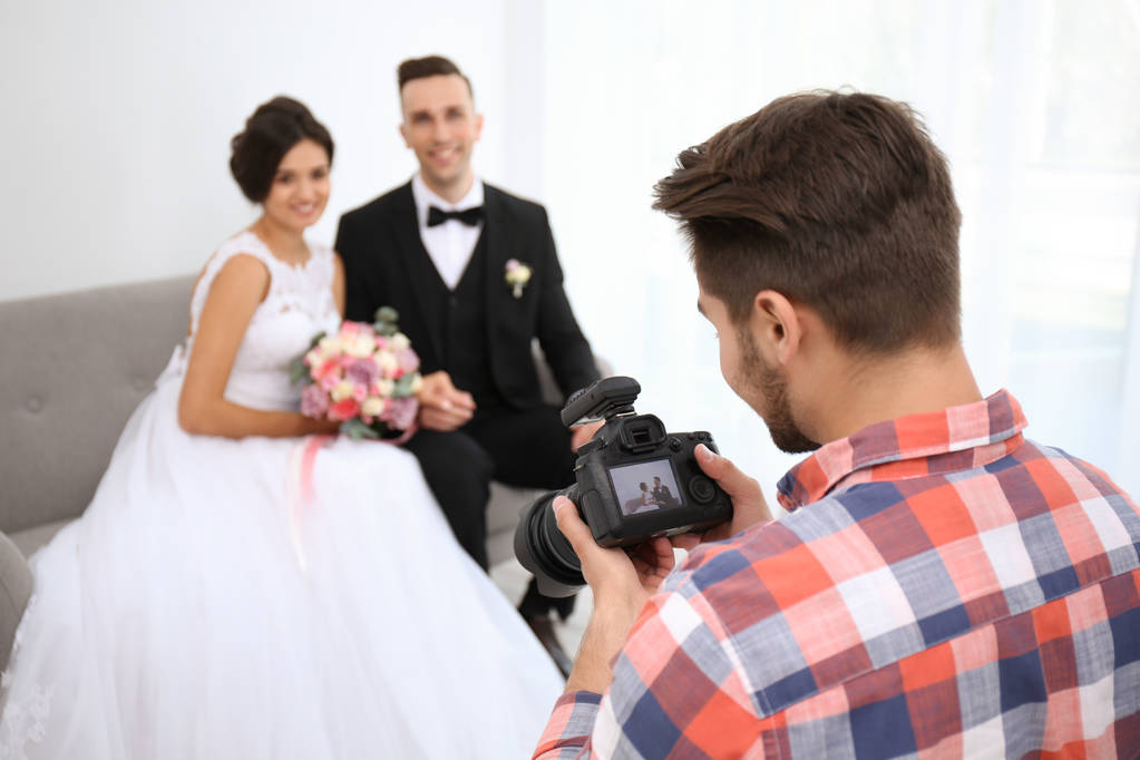 Επαγγελματίας φωτογράφος με κάμερα και το γαμήλιο ζεύγος στο στούντιο - Φωτογραφία, εικόνα