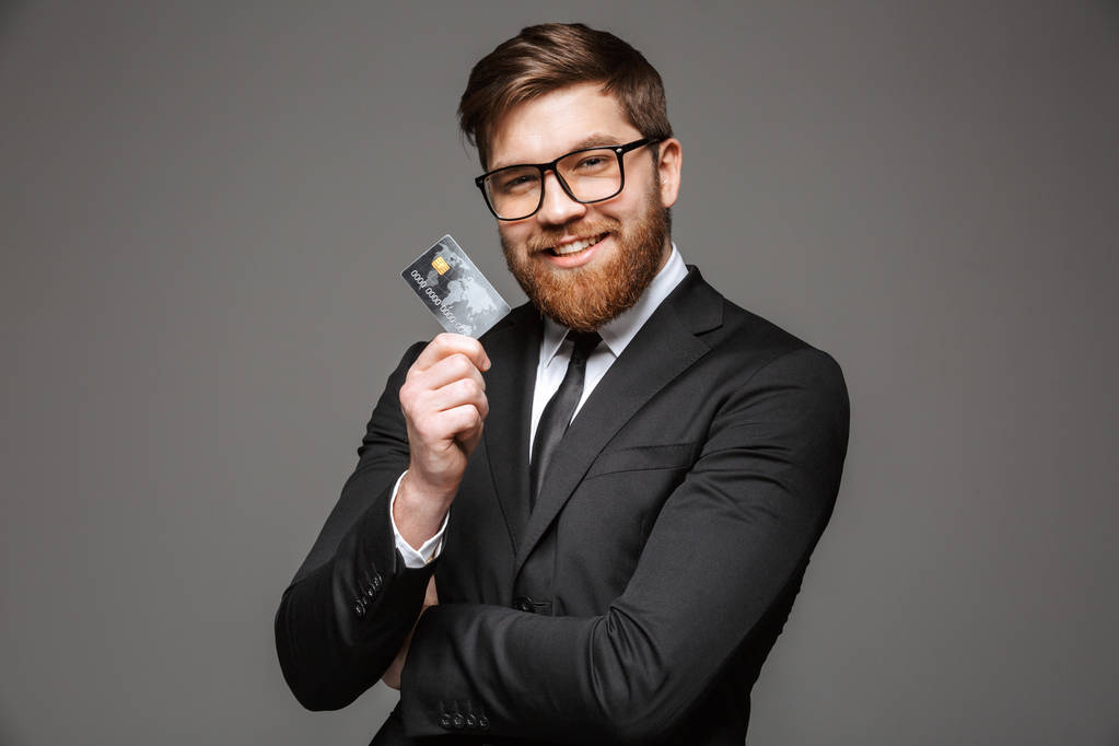 灰色の背景の上分離されたクレジット カードを持っている幸せな青年実業家の肖像画 - 写真・画像