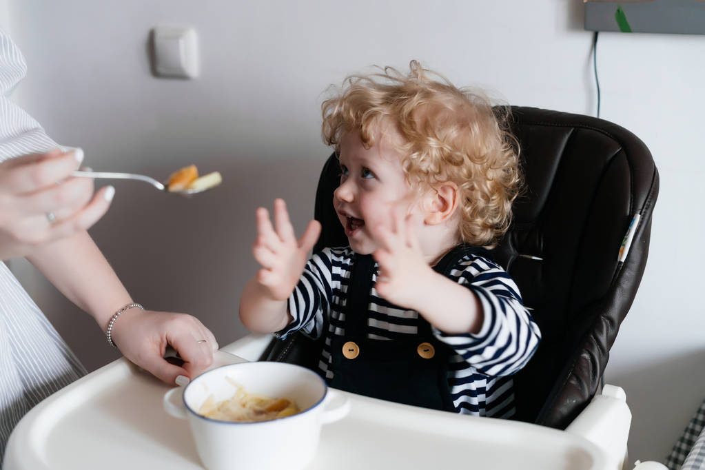 заботливая мать кормит своего маленького сына вкусным супом, на кухне, семейный ужин
 - Фото, изображение