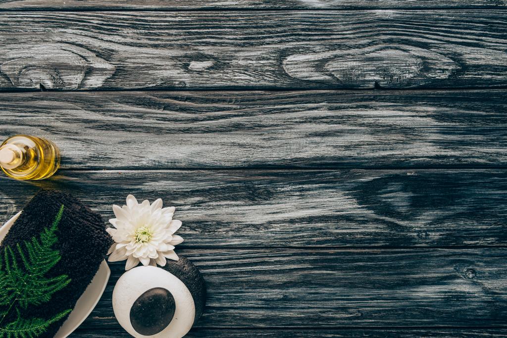 Draufsicht auf arrangierte Wellness- und Massageaccessoires mit Handtuch, Kieselsteinen, ätherischem Öl und Chrysanthemenblume auf Holzgrund - Foto, Bild