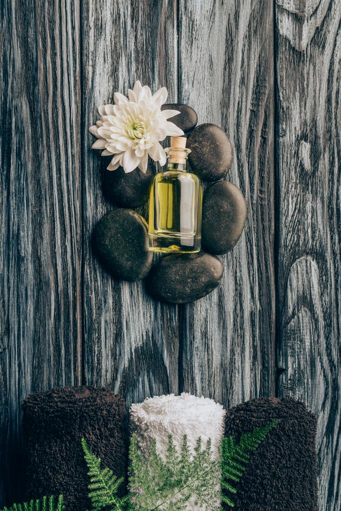 το Top view τοποθετημένα αιθέριο έλαιο μαύρο βότσαλο με χρυσάνθεμο το λουλούδι και πετσέτες για μασάζ και σπα σε ξύλινη επιφάνεια - Φωτογραφία, εικόνα