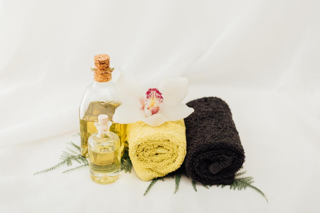 close up view of arrangement of spa treatment accessories with oil, towels and orchid flower on white background - Photo, Image