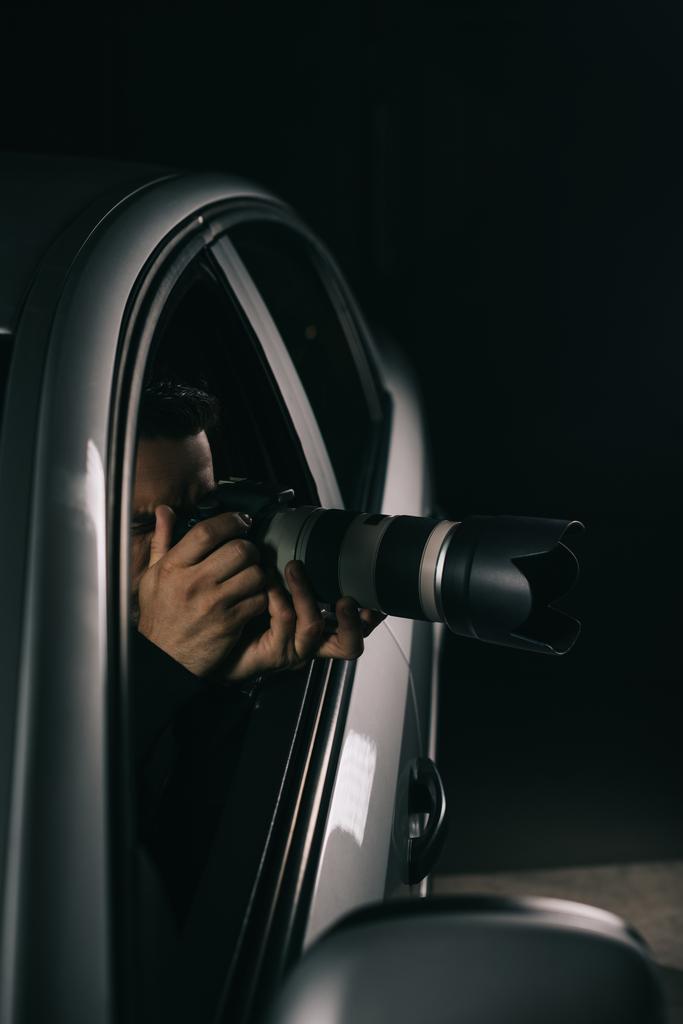 концентрированный мужчина-папарацци шпионит на камеру с объективом из своей машины
  - Фото, изображение