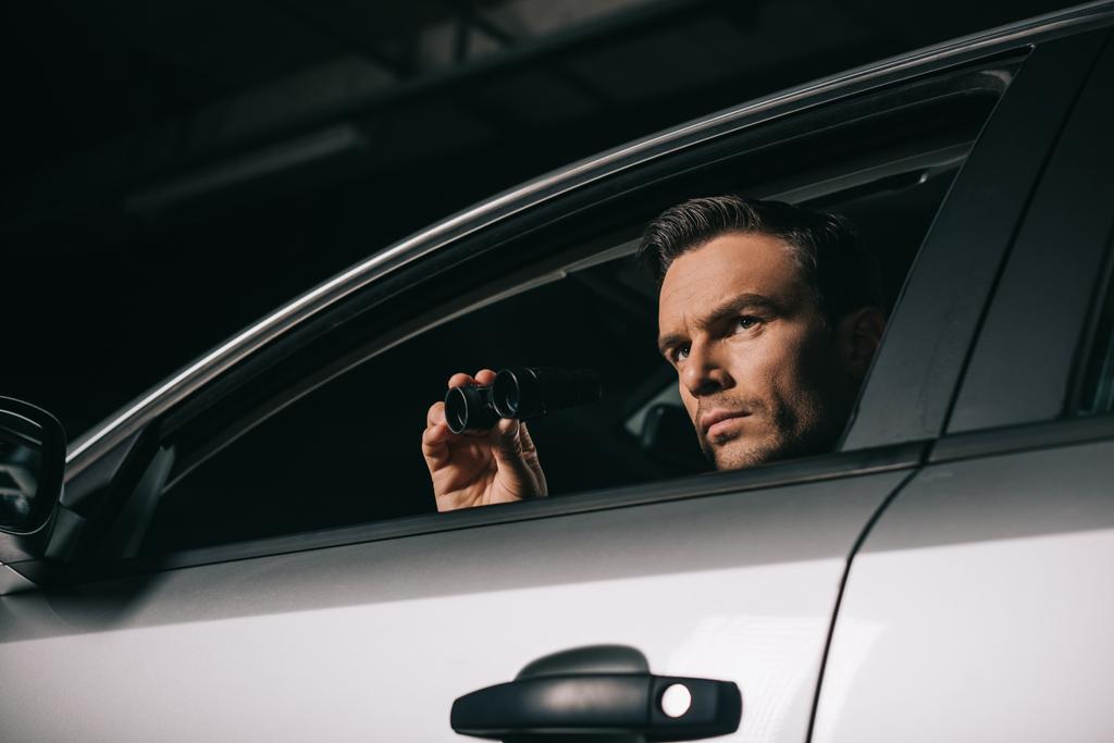 Tiefansicht männlicher Paparazzi bei der Überwachung mit Ferngläsern aus dem Auto  - Foto, Bild