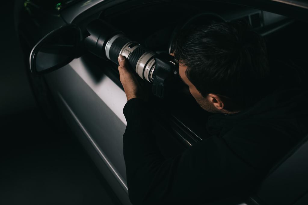 vista trasera del agente encubierto haciendo vigilancia por cámara con vidrio de objeto de su coche
  - Foto, Imagen