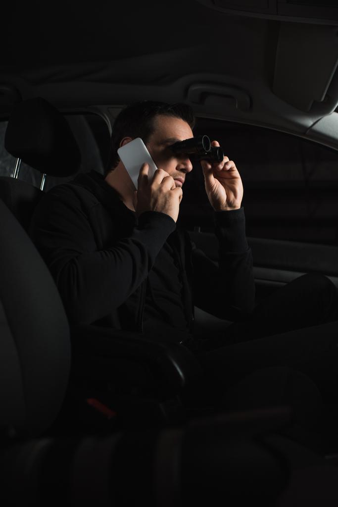 hombre haciendo vigilancia por prismáticos y hablando en smartphone en coche
  - Foto, Imagen