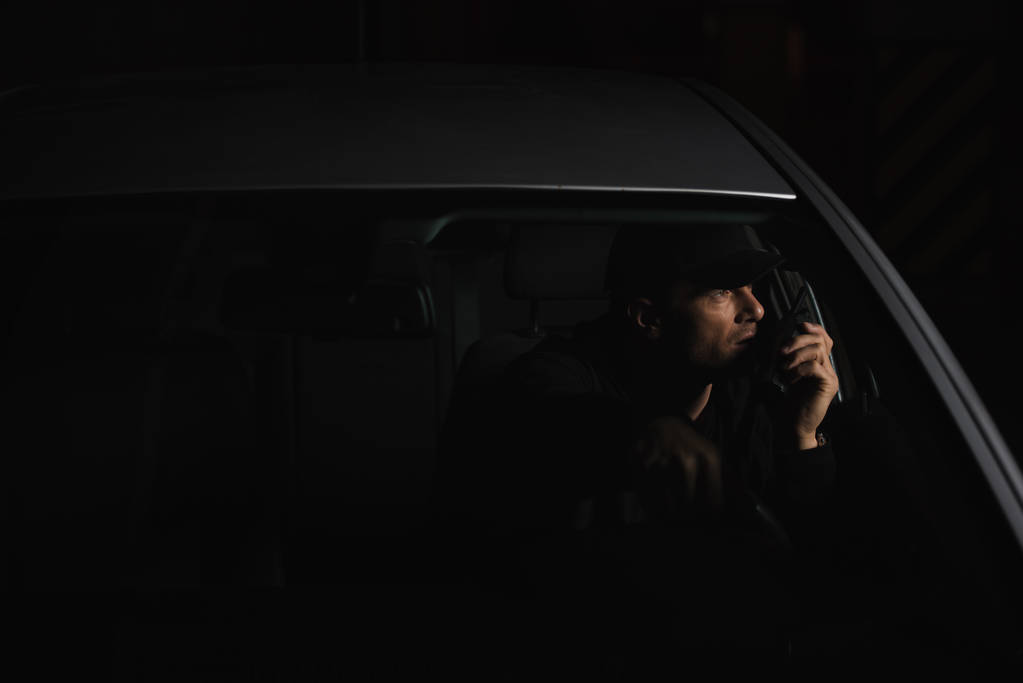 Widok z przodu mężczyzna prywatnego detektywa w cap za pomocą talkie walkie w samochodzie - Zdjęcie, obraz