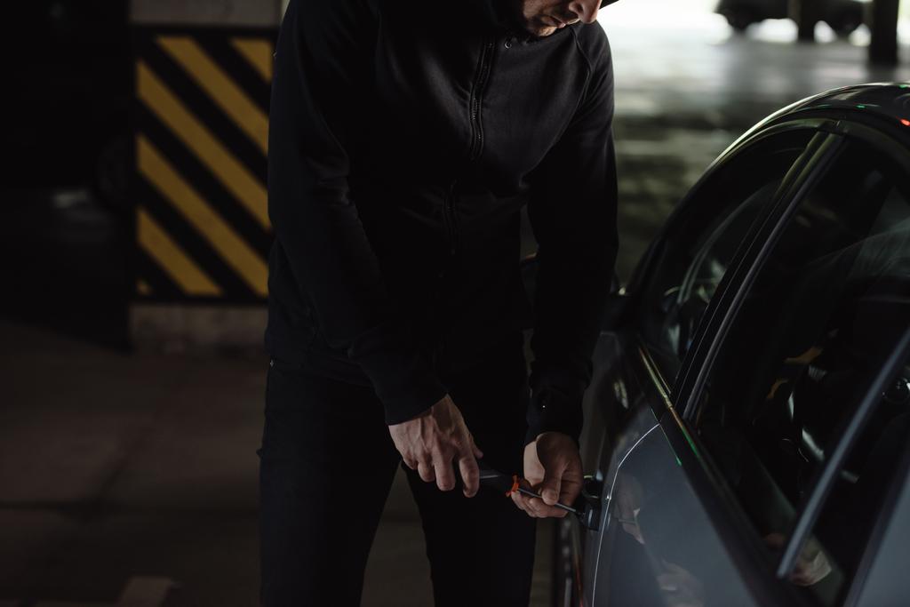 colpo ritagliato di rapinatore maschio in nero con cappuccio intrusione auto da cacciavite
  - Foto, immagini