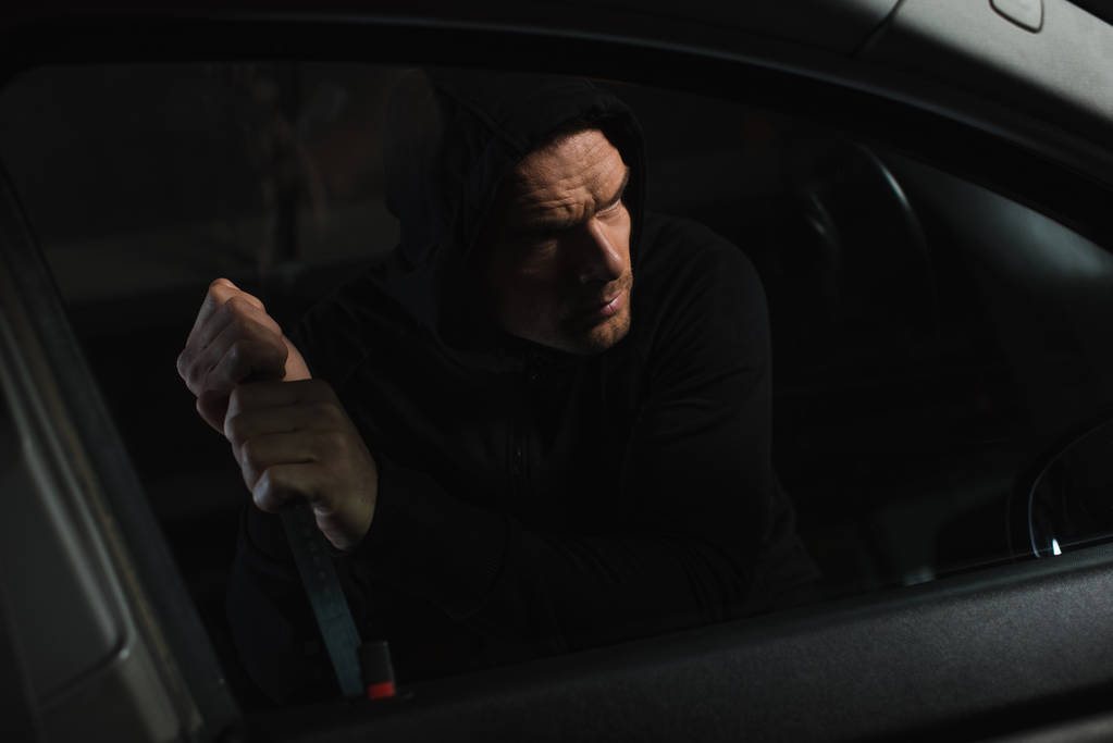 σοβαρή ανδρική ληστής σε μαύρο hoodie απρόσκλητος αυτοκίνητο με λοστό - Φωτογραφία, εικόνα