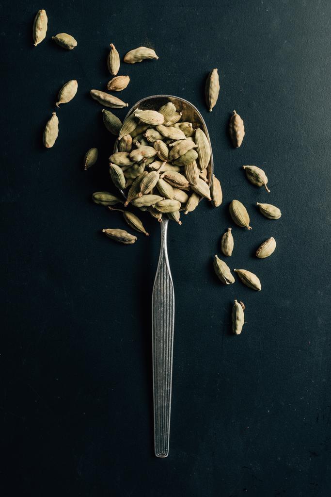 верхний вид семян кардамона на ложке и темном столе
 - Фото, изображение
