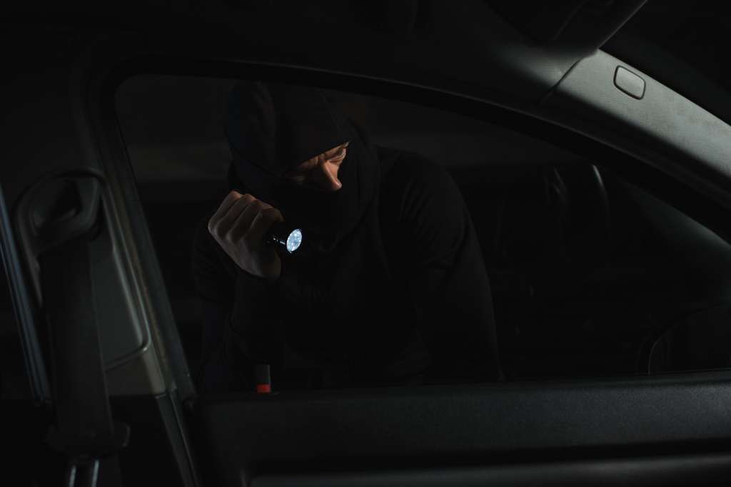 ladrón de sexo masculino en pasamontañas negro con linterna mirando hacia el coche
  - Foto, imagen