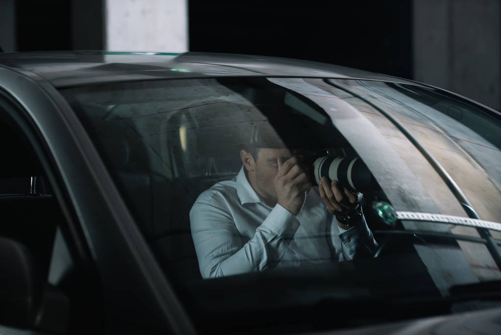 Mies yksityisetsivä tekee valvontaa kameralla objekti lasi autostaan
 - Valokuva, kuva