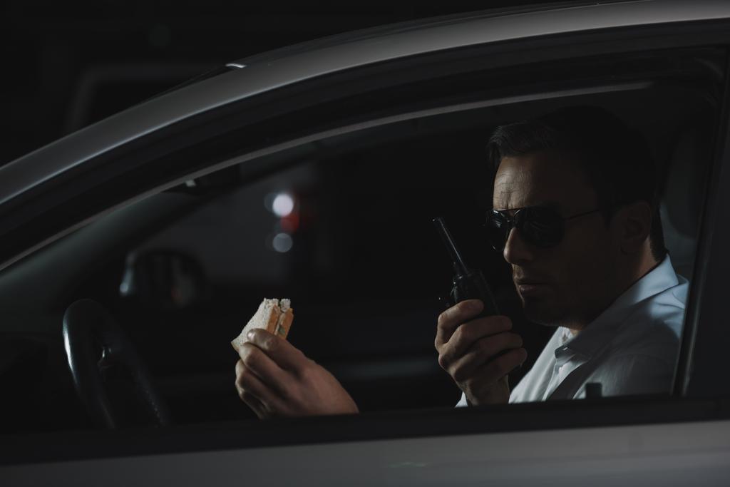 αρσενικό μυστικός πράκτορας σε γυαλιά ηλίου το γεύμα και γουόκι τόκι που χρησιμοποιεί στο αυτοκίνητο - Φωτογραφία, εικόνα