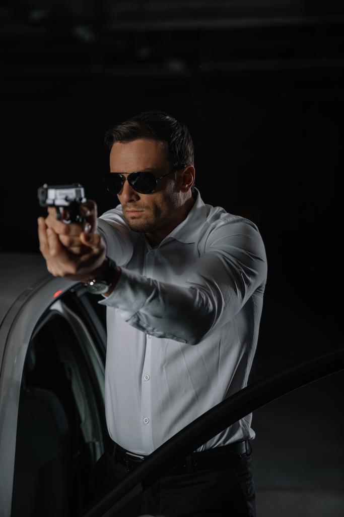 Frontansicht eines verdeckten männlichen Agenten mit Sonnenbrille, der mit einer Waffe zielte  - Foto, Bild