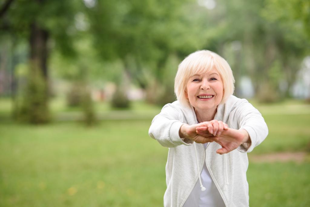 elderly sportswoman exercising on green lawn in park - Photo, Image