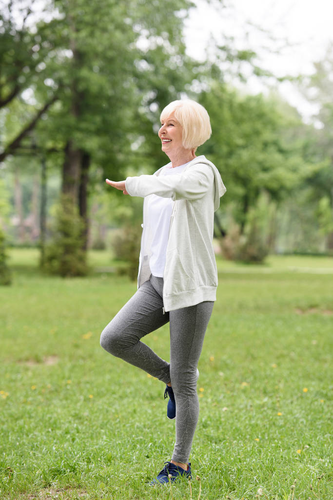 s úsměvem starší sportovkyně cvičení na zelené trávě v parku - Fotografie, Obrázek