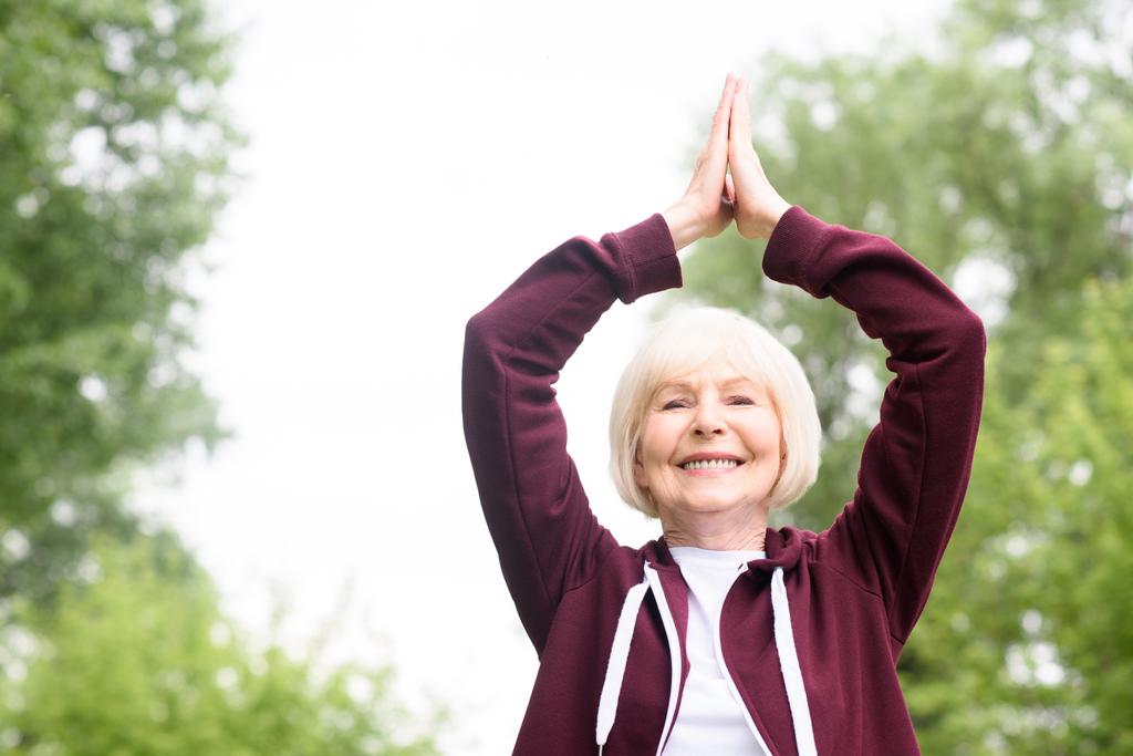 glimlachend senior vrouw praktizerende yoga in park - Foto, afbeelding