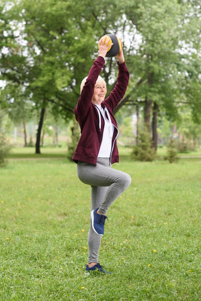 uśmiechnięta kobieta senior szkolenia z piłką w parku - Zdjęcie, obraz