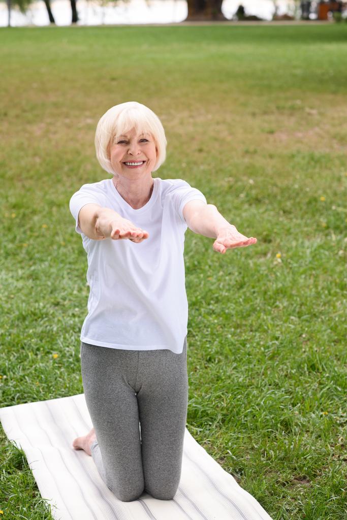 šťastná starší žena cvičí jóga podložku na zeleném trávníku - Fotografie, Obrázek