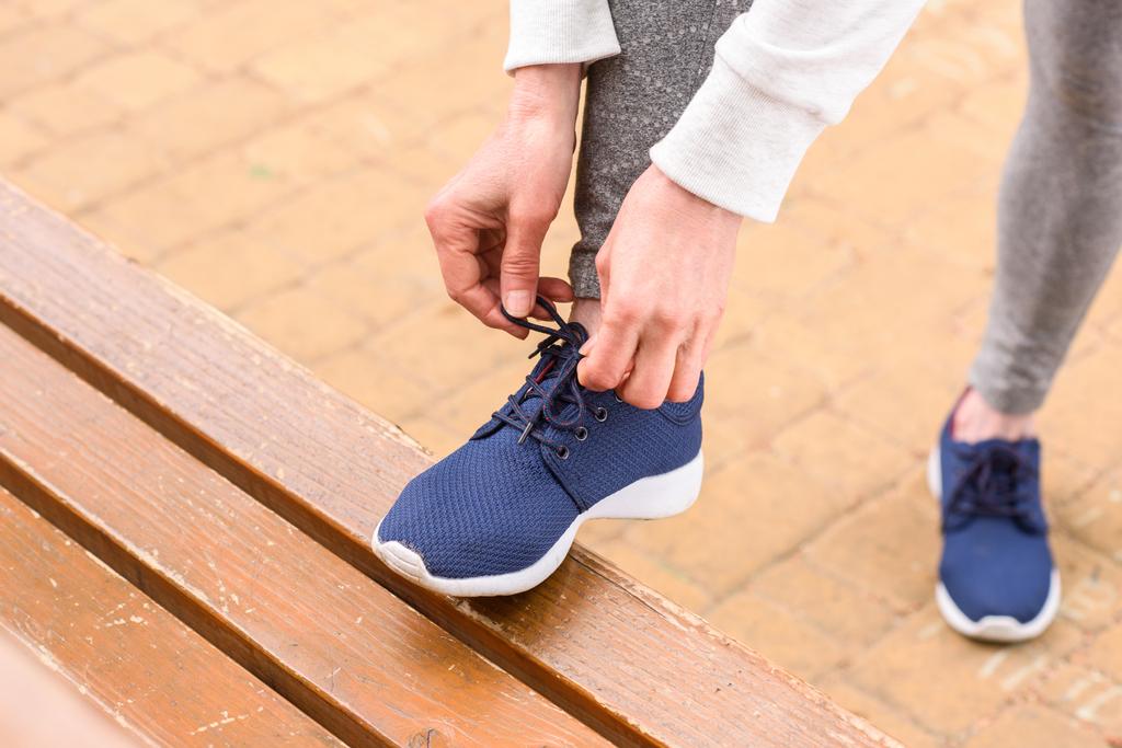 cropped view of sportswoman tying shoelaces on blue sneakers - Photo, Image