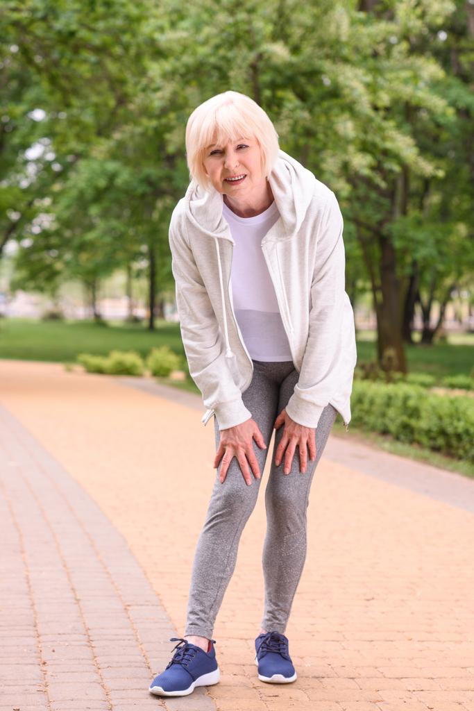ouderen Sportvrouw met knie pijn staande in park - Foto, afbeelding