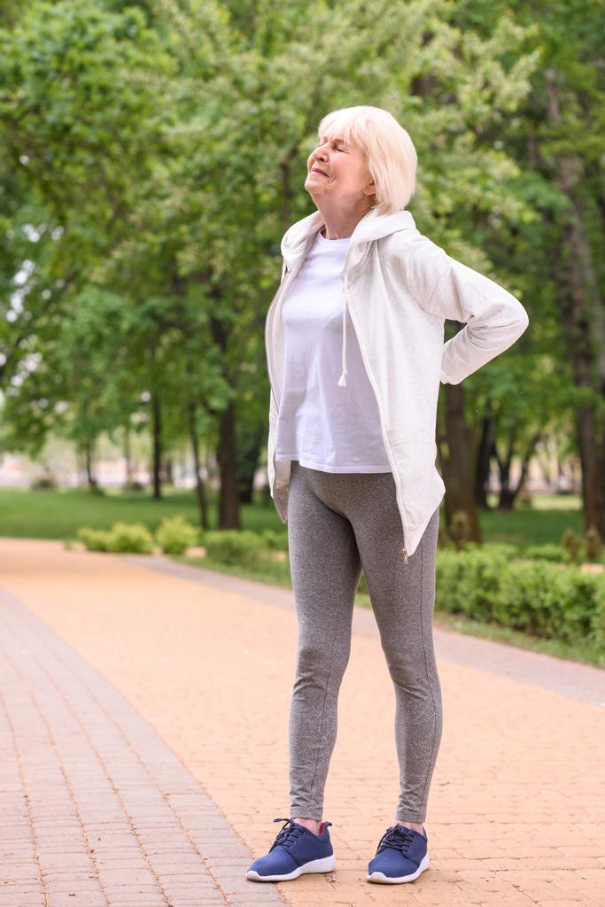 Ältere Sportlerin mit Rückenschmerzen steht im Park - Foto, Bild