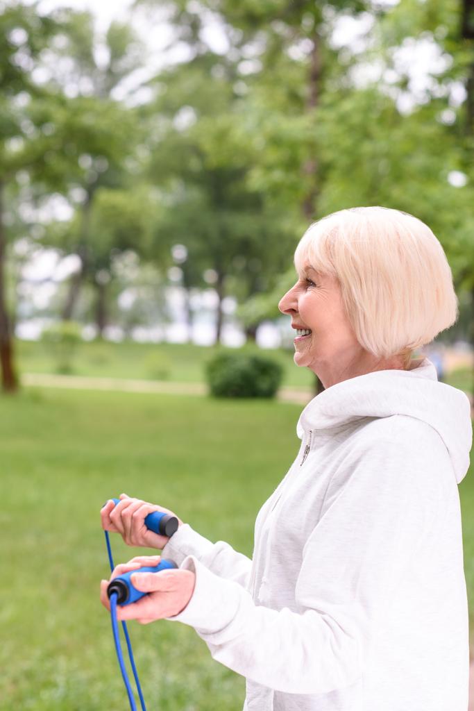 счастливая старшая спортсменка тренируется с скакалкой в парке
 - Фото, изображение