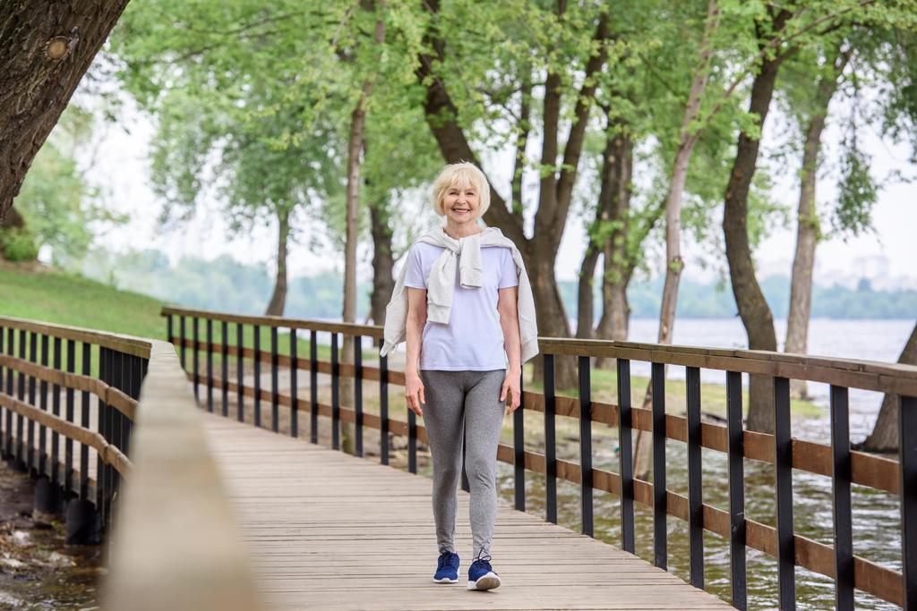 anziana in abbigliamento sportivo che cammina sul sentiero in legno nel parco
 - Foto, immagini