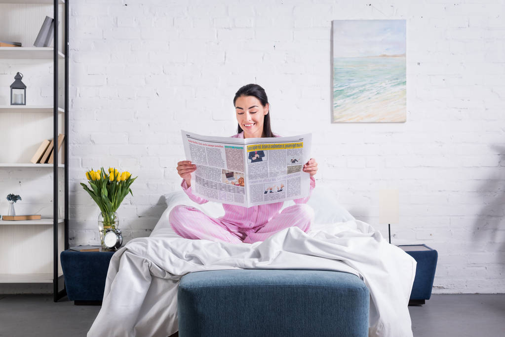 自宅のベッドで新聞を読んでのパジャマを着て笑顔の女性 - 写真・画像