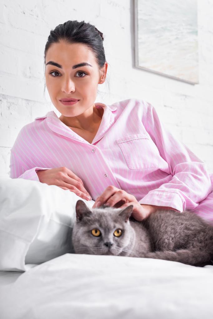 portrait of woman with britain shorthair cat resting on bed at home - Photo, Image