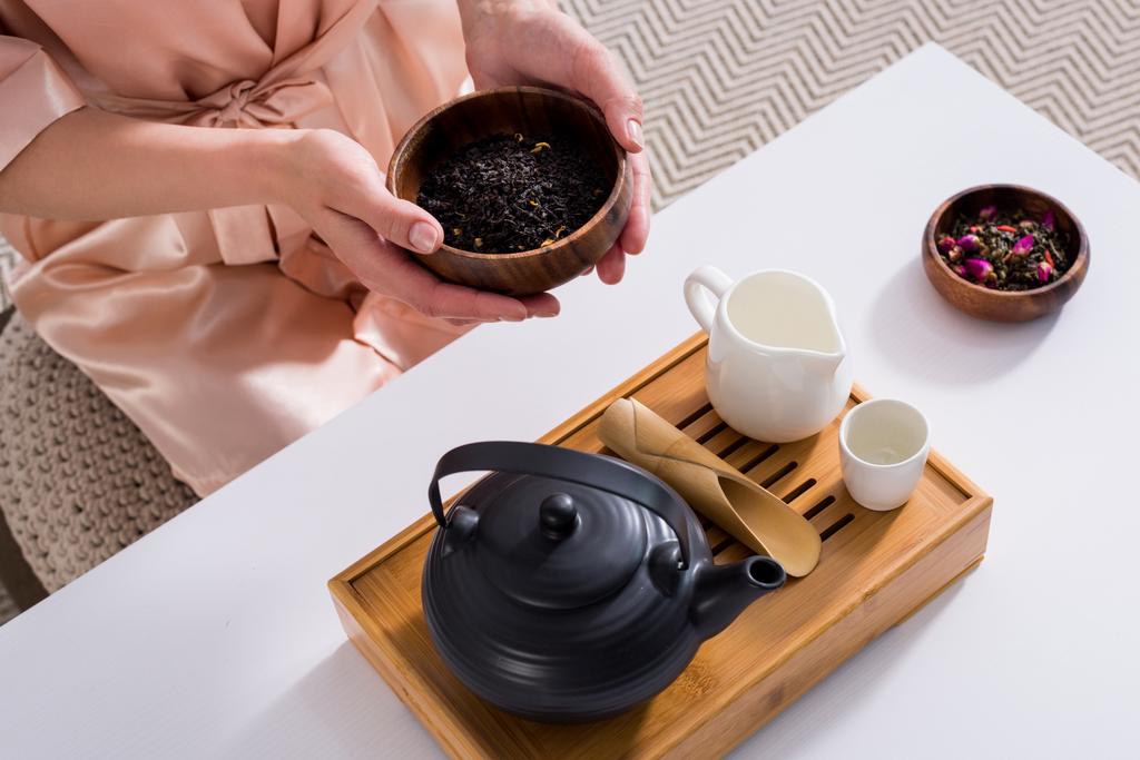 tiro cortado de mulher segurando tigela de madeira com chá preto em mãos de manhã em casa
 - Foto, Imagem