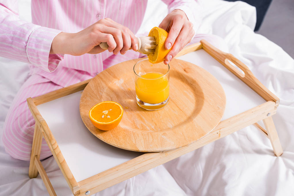 vista parcial de la mujer con pestle de madera haciendo jugo de naranja fresco en la cama en la mañana en casa
 - Foto, Imagen