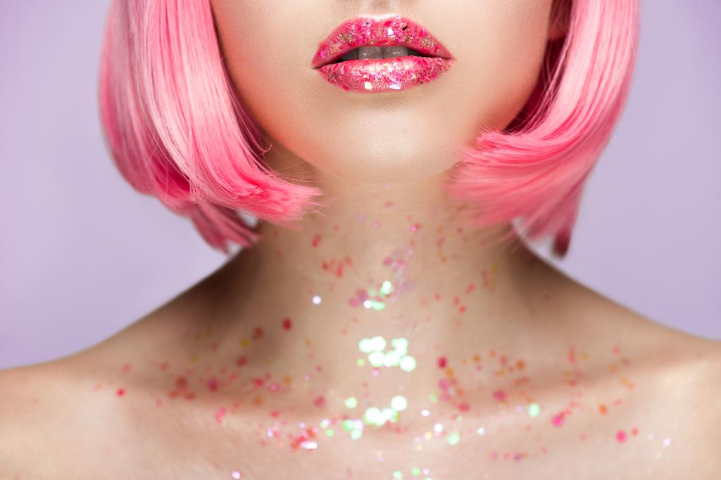 περικομμένη εικόνα γυναίκας με ροζ μαλλιά και λάμψη στα χείλη και το λαιμό που απομονώνονται σε βιολετί - Φωτογραφία, εικόνα