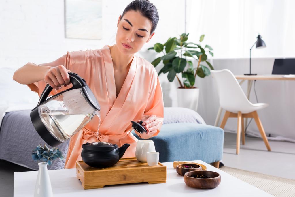 attraktive Frau im Seidenbademantel, die Tee kocht, während sie morgens zu Hause Teezeremonie hat - Foto, Bild