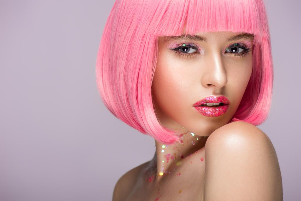 ελκυστική γυναίκα που ποζάρει με ροζ μαλλιά και λάμψη στο πρόσωπο απομονωμένες σε βιολετί - Φωτογραφία, εικόνα