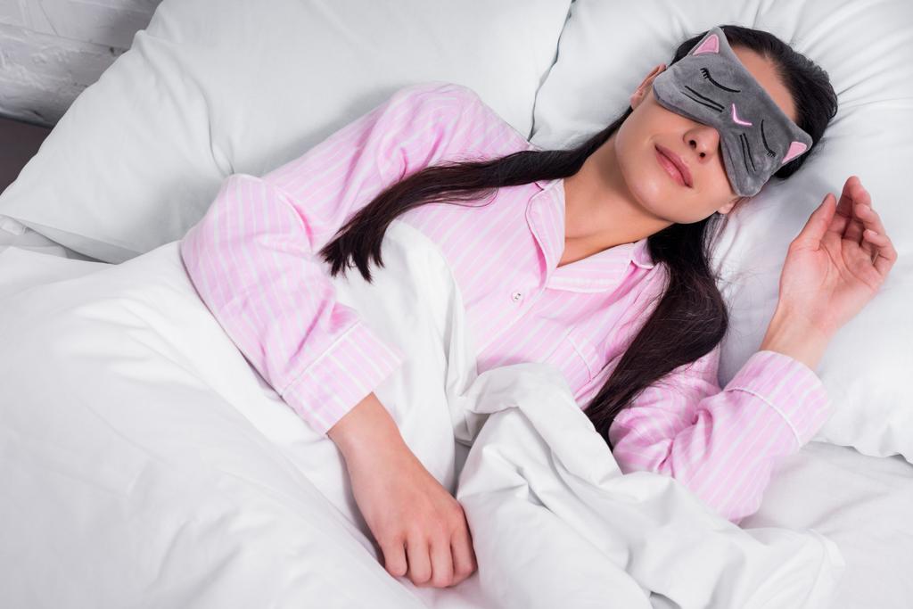ピンクのパジャマと自宅のベッドで寝ているアイマスクで女性の肖像 - 写真・画像
